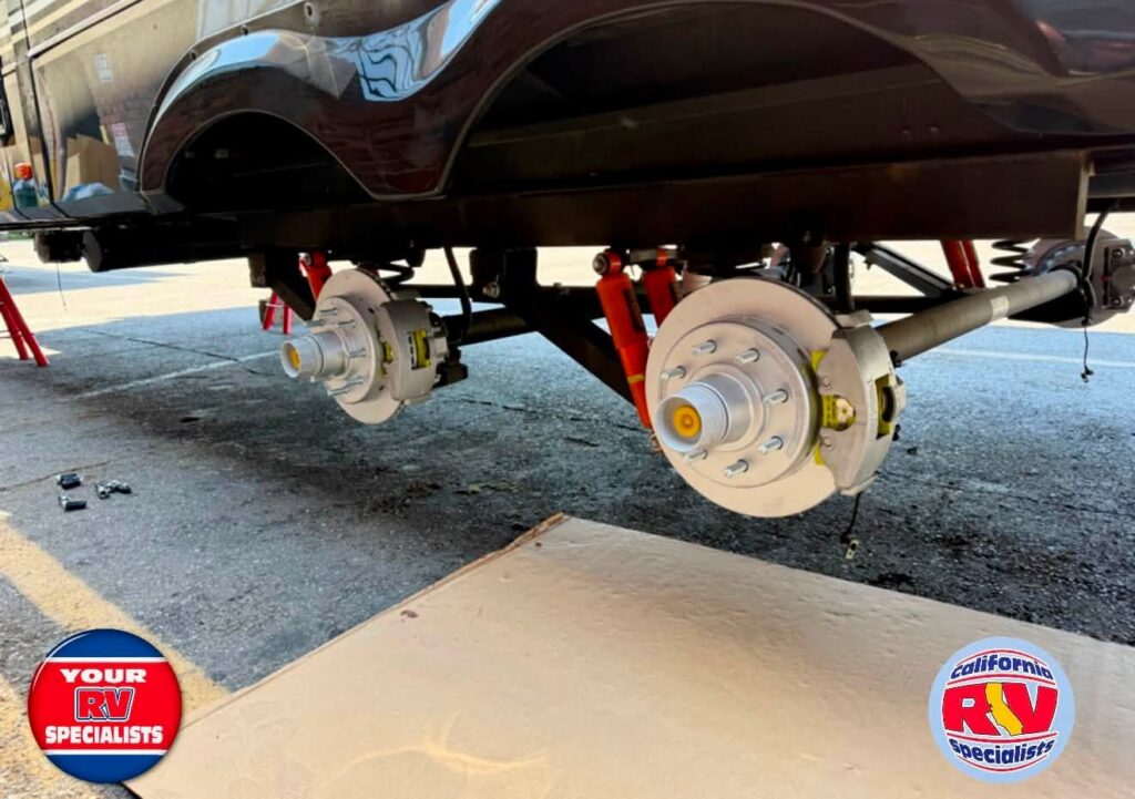 RV undergoing brake maintenance with wheels removed, showing exposed brake rotors and wheel hubs undercarriage on stands