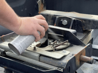 Close-up of a hand spraying lubricant onto a rusty trailer hitch frame.