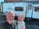 Man and young child pose for a selfie in front of a large white travel trailer with 'IMAGINE' branding in a dealership lot.
