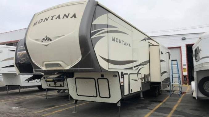 A large Montana fifth-wheel RV parked in a lot, with a ladder and other trailers nearby. The front cap and side graphics are visible, including the word Montana on the front and side panels.