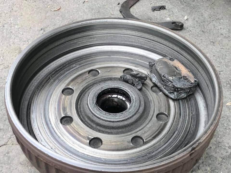 Magnet failure - California RV Specialists Steel car wheel rim with a central bore and six lug holes, resting on a rough concrete surface with a rock on top of it.