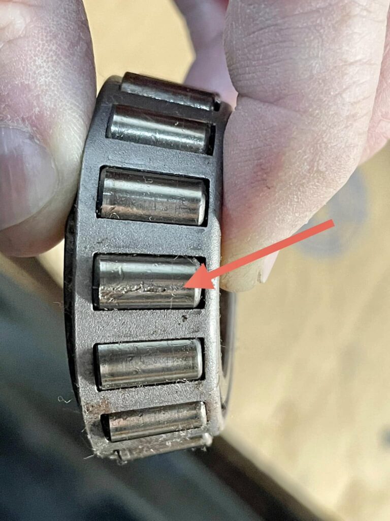 Wheel Bearing pitting - California RV Specialists Close-up of a black plastic roller mechanism with multiple metal rollers being held between fingers.