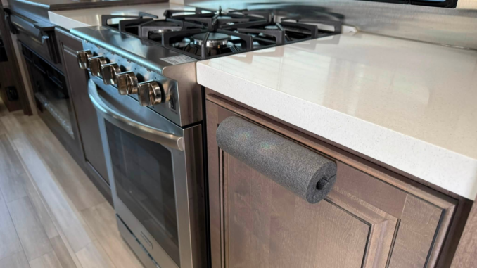 Stainless steel gas range with four burners in a compact kitchen, next to a white countertop and window with blinds.