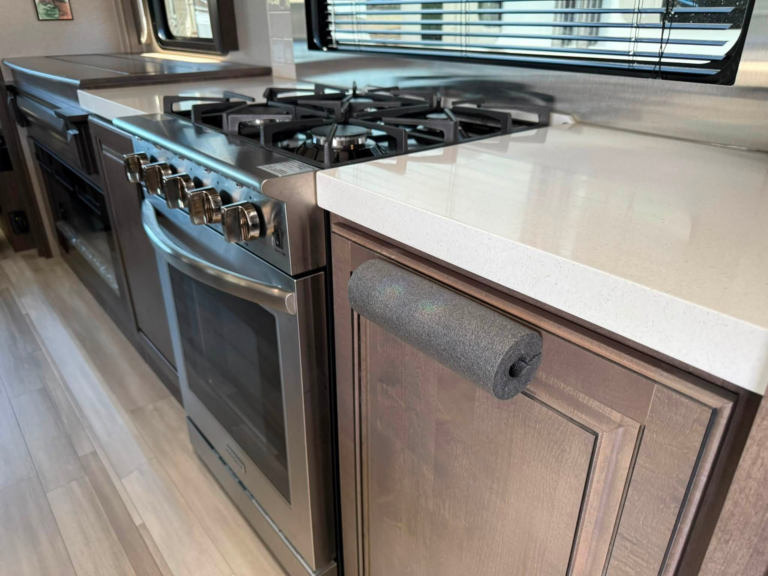 Stainless steel gas range with four burners in a compact kitchen, next to a white countertop and window with blinds.