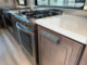 Stainless steel gas range with four burners in a compact kitchen, next to a white countertop and window with blinds.