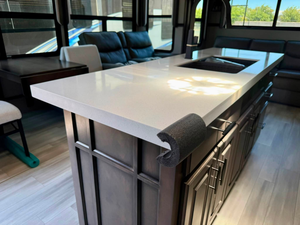 RV kitchen island with a white countertop and built-in sink, dark cabinets, and a seating area visible in the background