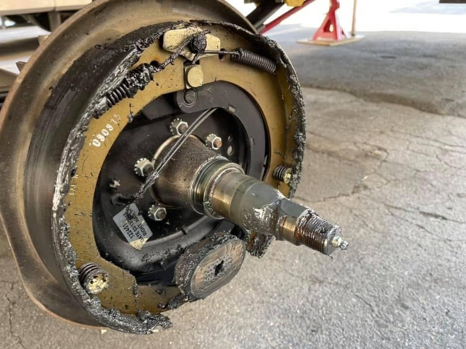 Close-up of a vehicle wheel hub with the brake drum removed, exposing the axle shaft and surrounding damaged brake components with signs of wear and grime.