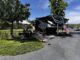 Large black-and-white Solitude RV parked at a campsite with American flags, canopy, and bicycles in a sunny park.