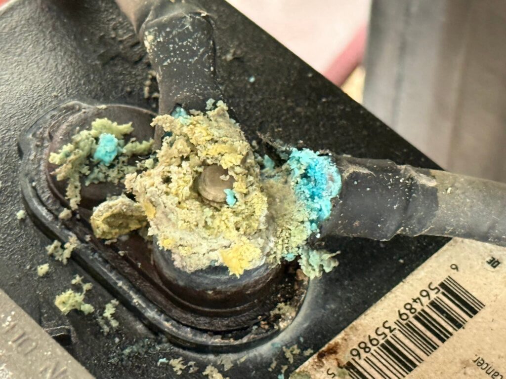 Close-up of a dark, corroded metal surface with turquoise and yellow mineral deposits, next to a ruler showing measurements in centimeters and millimeters.