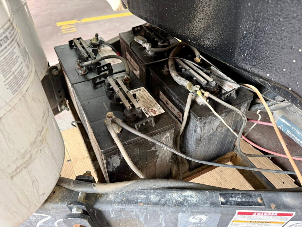 Two large lead-acid batteries with connected cables in a dusty machinery compartment.