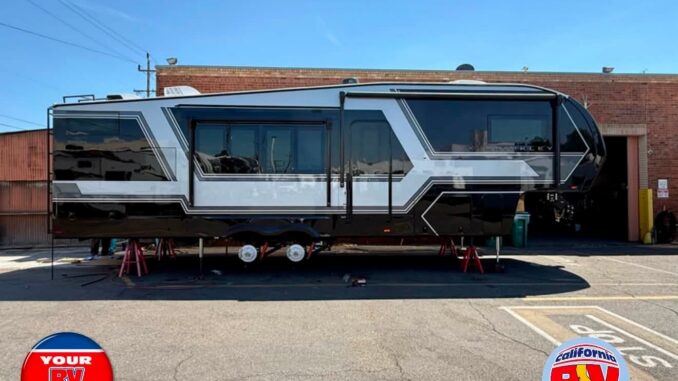 Large modern travel trailer on leveling jacks outside a service shop, with branding logos in the corners: 'Your RV Specialists' and 'California RV Specialists'