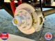Close-up of a RV trailer wheel hub with brake rotor and caliper, showing lug studs and a yellow center cap on a paved surface.