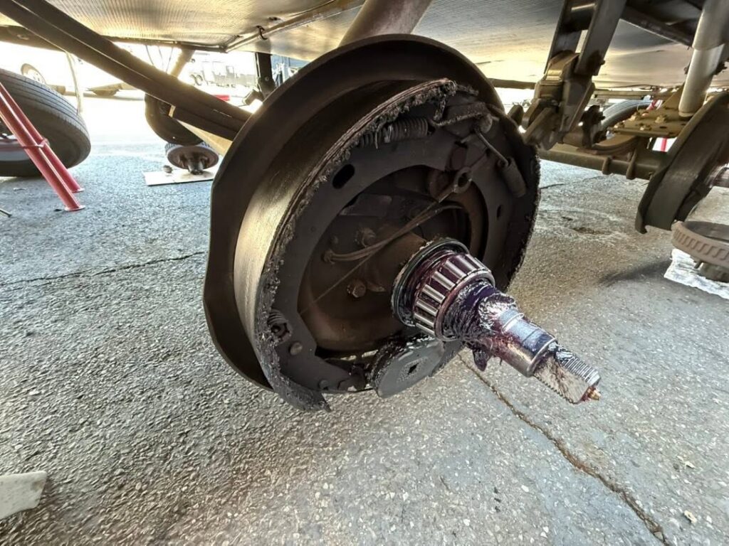 Wheel hub with brake drum removed; rusted drive axle protruding from the hub, showing torn boot and exposed splines under the vehicle on a paved surface.